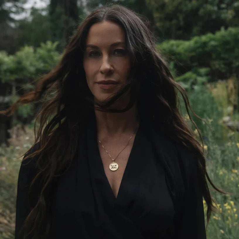 Woman with long, dark hair wearing a black dress and a gold pendant necklace