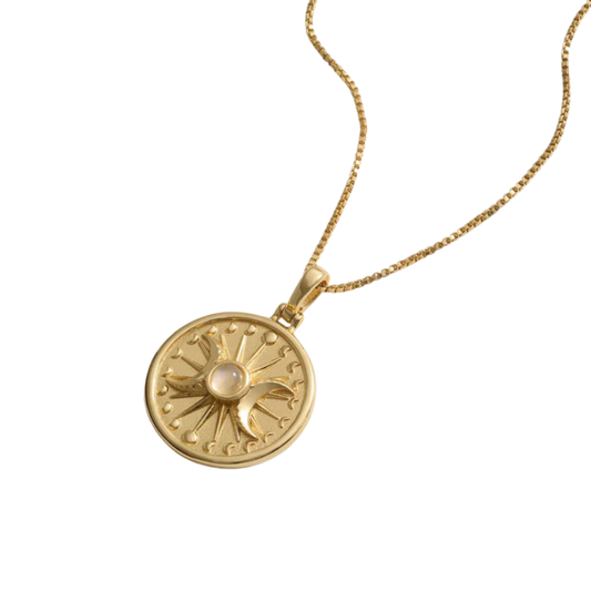 Gold necklace with a circular pendant featuring a sun, moon, and a central pink gemstone.