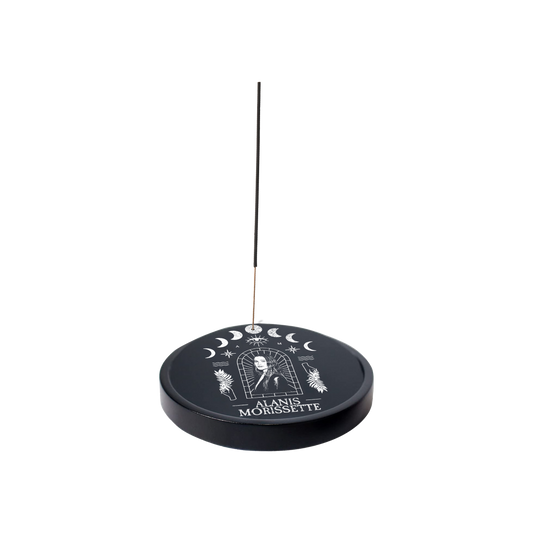 Circular incense holder with celestial designs and ’Alanis Morissette’ text, featuring a thin incense stick.